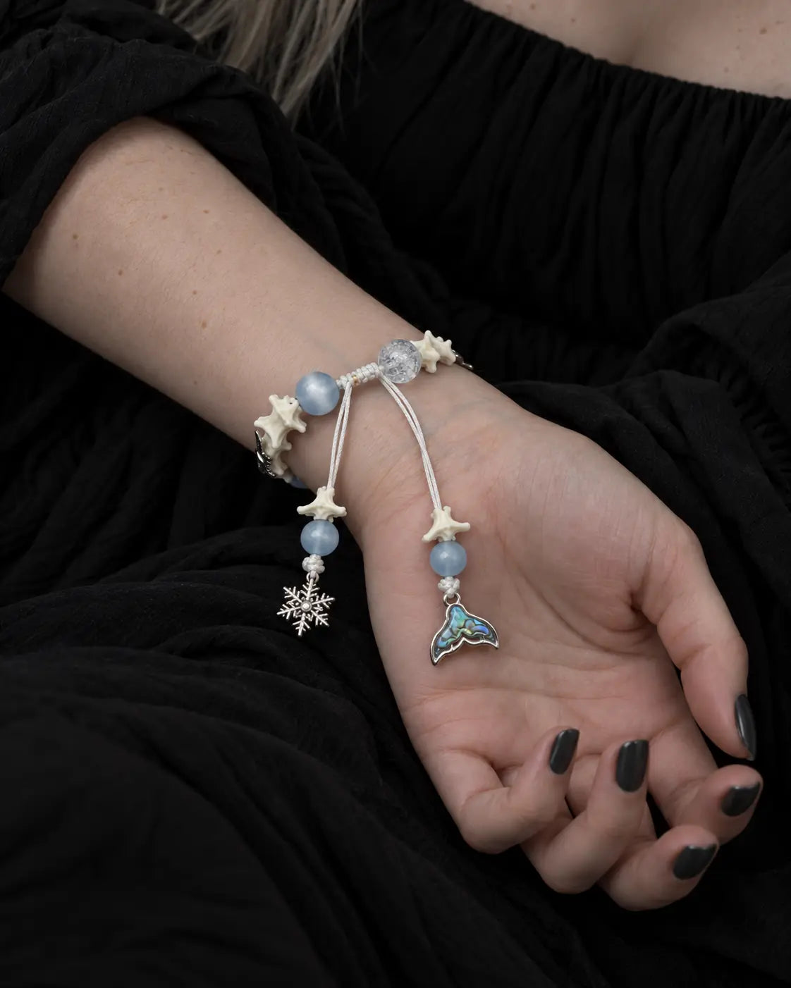 Palm-up view of the Frost Tide snake bone bracelet showing its white sliding knot, snowflake and iridescent tail charms