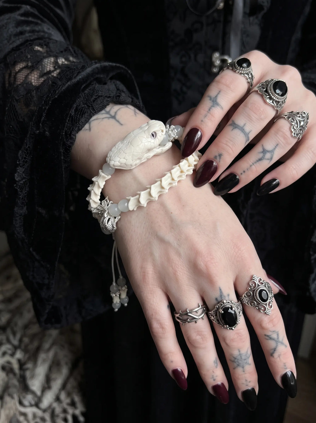 Ghostcoil Snake Bone Bracelet, close-up of stacked white vertebrae bracelet worn with gothic silver rings