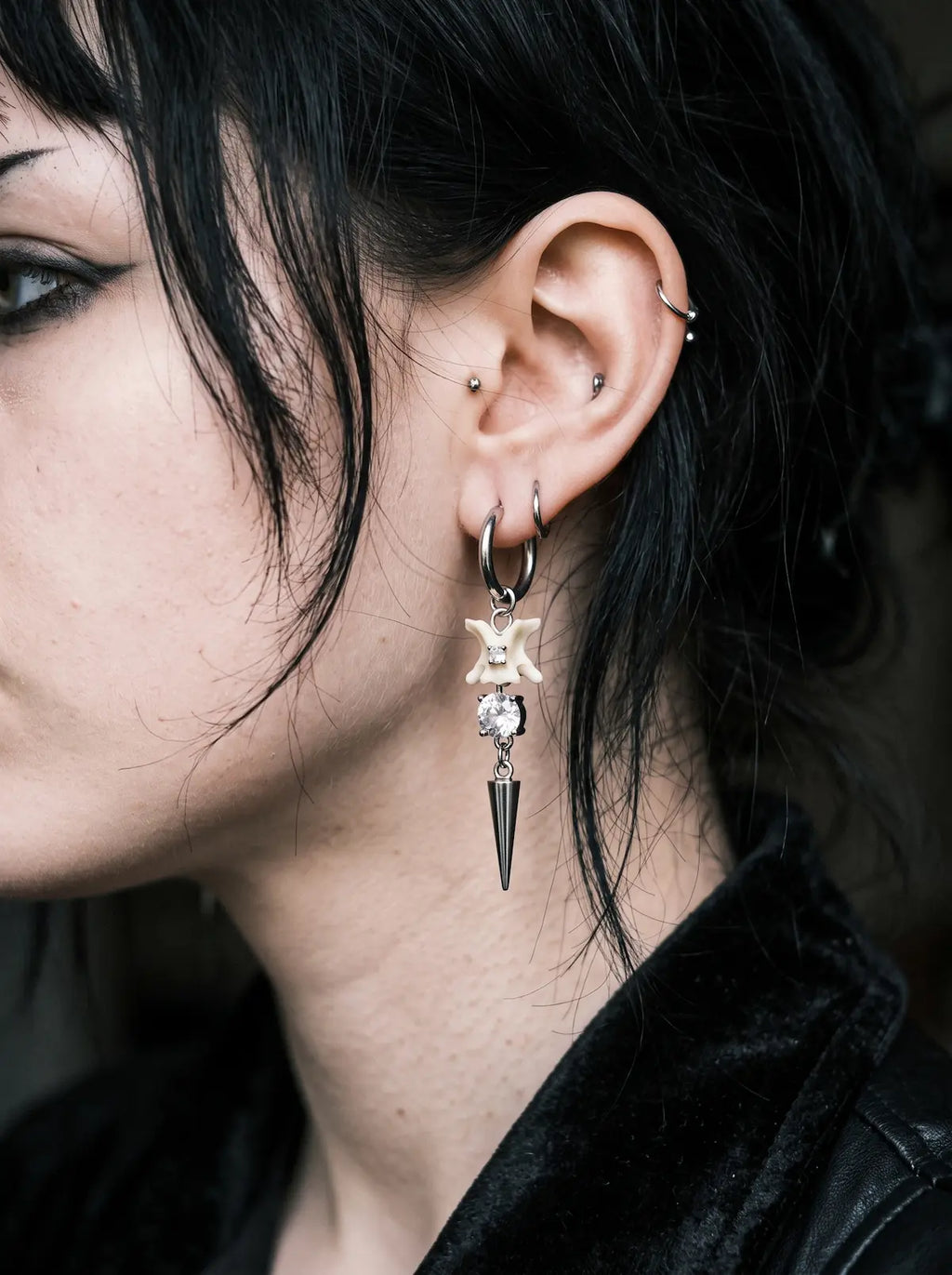 Glimmerthorn Snake Bone Earrings, close-up of pale snake bone and star earring hanging beside dark hair