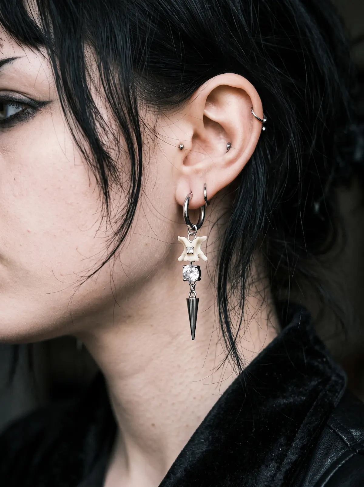 Glimmerthorn Snake Bone Earrings, close-up of pale snake bone and star earring hanging beside dark hair