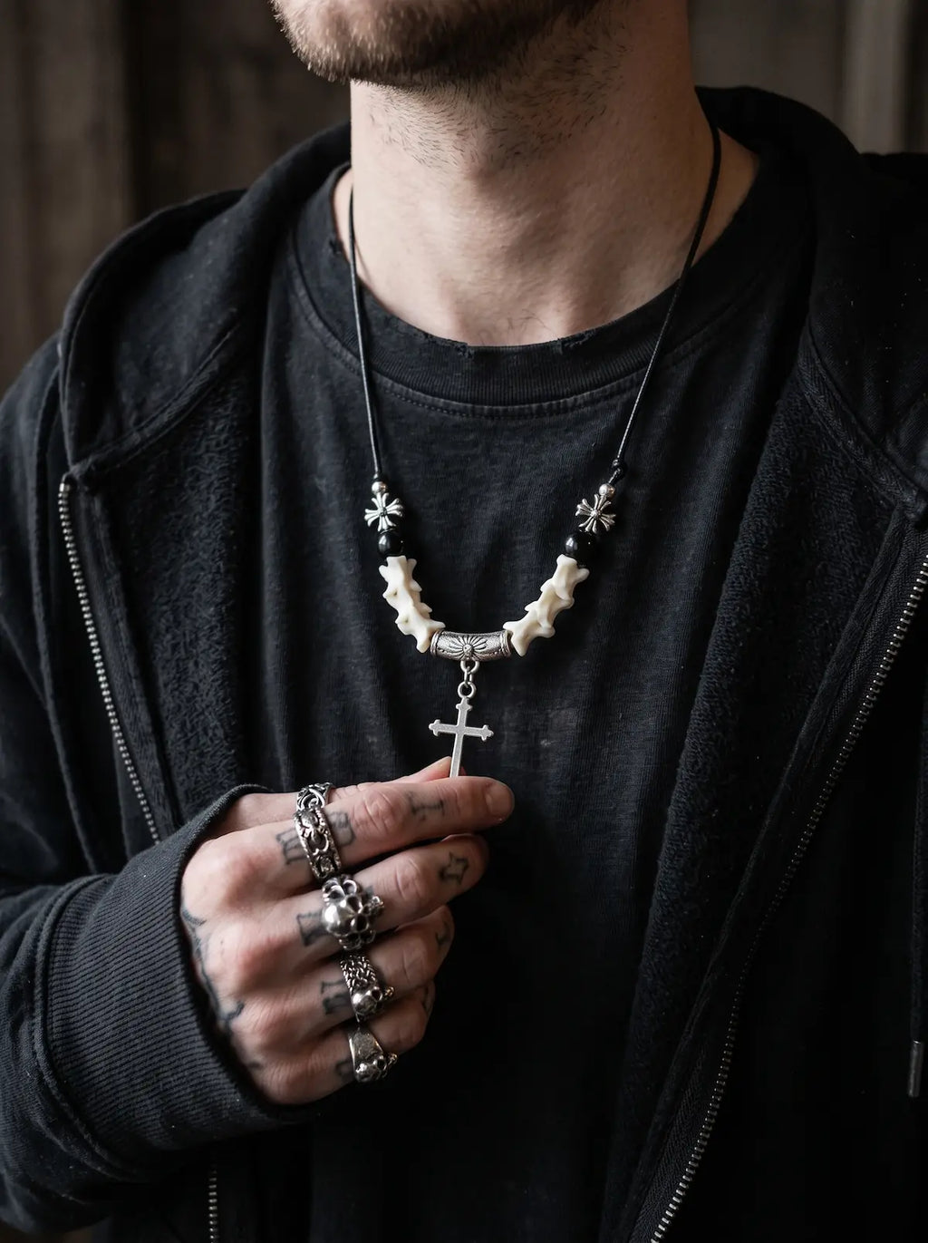 Gravecross Snake Bone Necklace, snake bone cross necklace worn over a dark shirt with silver rings
