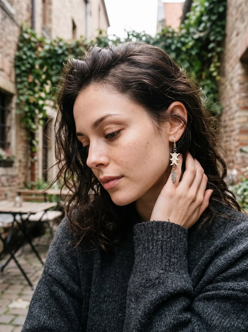 Gravefeather snake bone earring worn outdoors with a hand holding the hair away from the ear