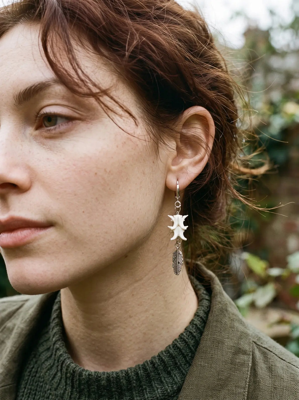 Close-up of a Gravefeather earring showing white snake vertebrae above a silver-tone feather