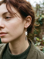 Close-up of a Gravefeather earring showing white snake vertebrae above a silver-tone feather