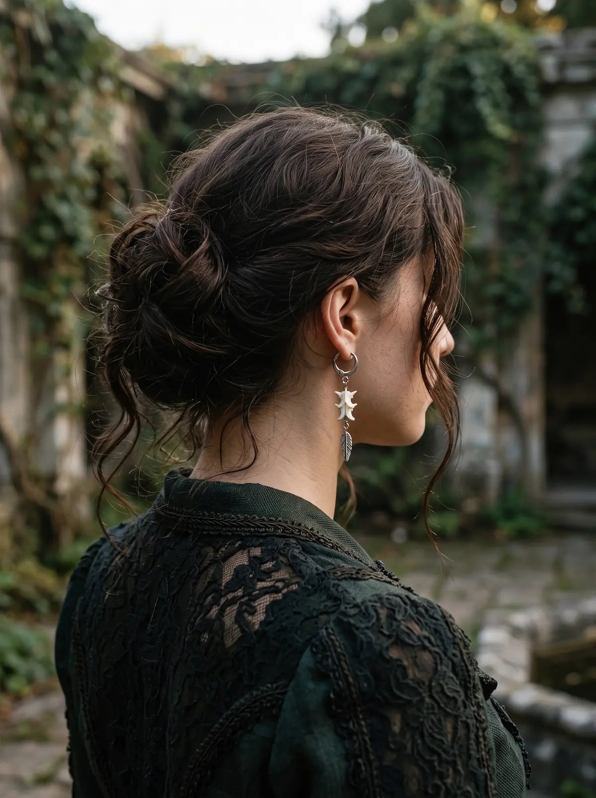 Rear three-quarter view of a Gravefeather snake bone earring worn with the hair pinned up