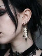 Gravefork Snake Bone Earrings, pale spine earring with pointed dark metal pendant, shown on the ear from the side