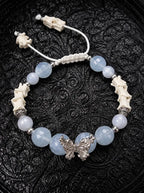 Icewing snake bone bracelet with pale blue beads, a silver-tone butterfly and white adjustable cords on black fabric