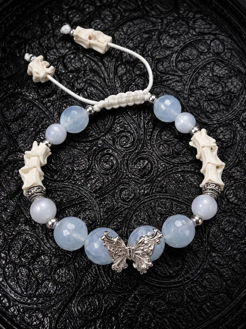 Icewing snake bone bracelet with pale blue beads, a silver-tone butterfly and white adjustable cords on black fabric