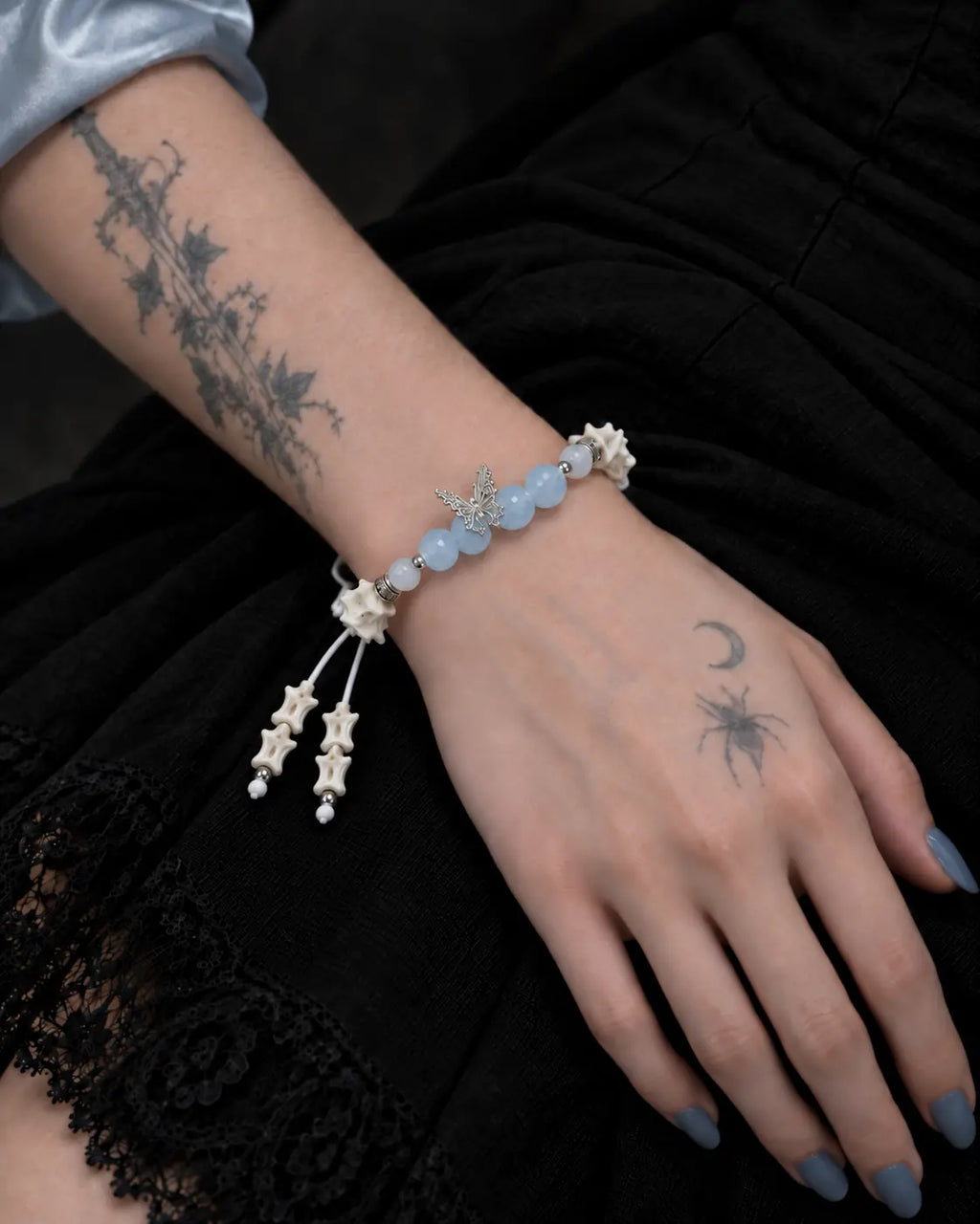 Icewing snake bone bracelet on a hand resting against black lace, with pale blue beads across the wrist