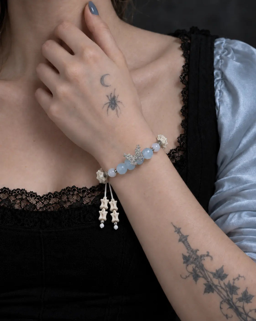 Icewing snake bone bracelet worn with the hand at the collarbone, highlighting its pale blue beads and butterfly