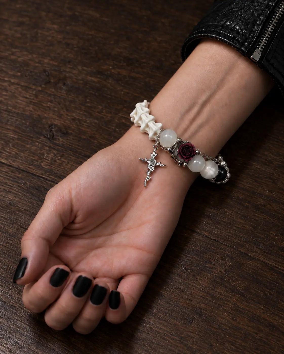 Ivory Thorn Rose snake bone bracelet on a palm-up wrist resting on wood, showing its rose and cross charms