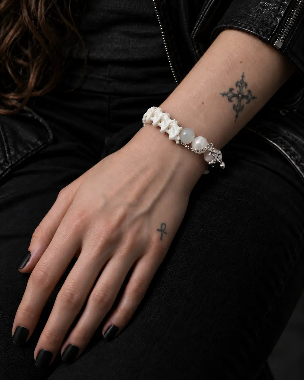 Ivory Thorn Rose snake bone bracelet on a hand resting on black trousers, with the vertebrae facing upward