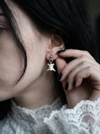 Ivory Vertebra Drop snake bone stud earring worn above a white lace collar with a hand beside the ear