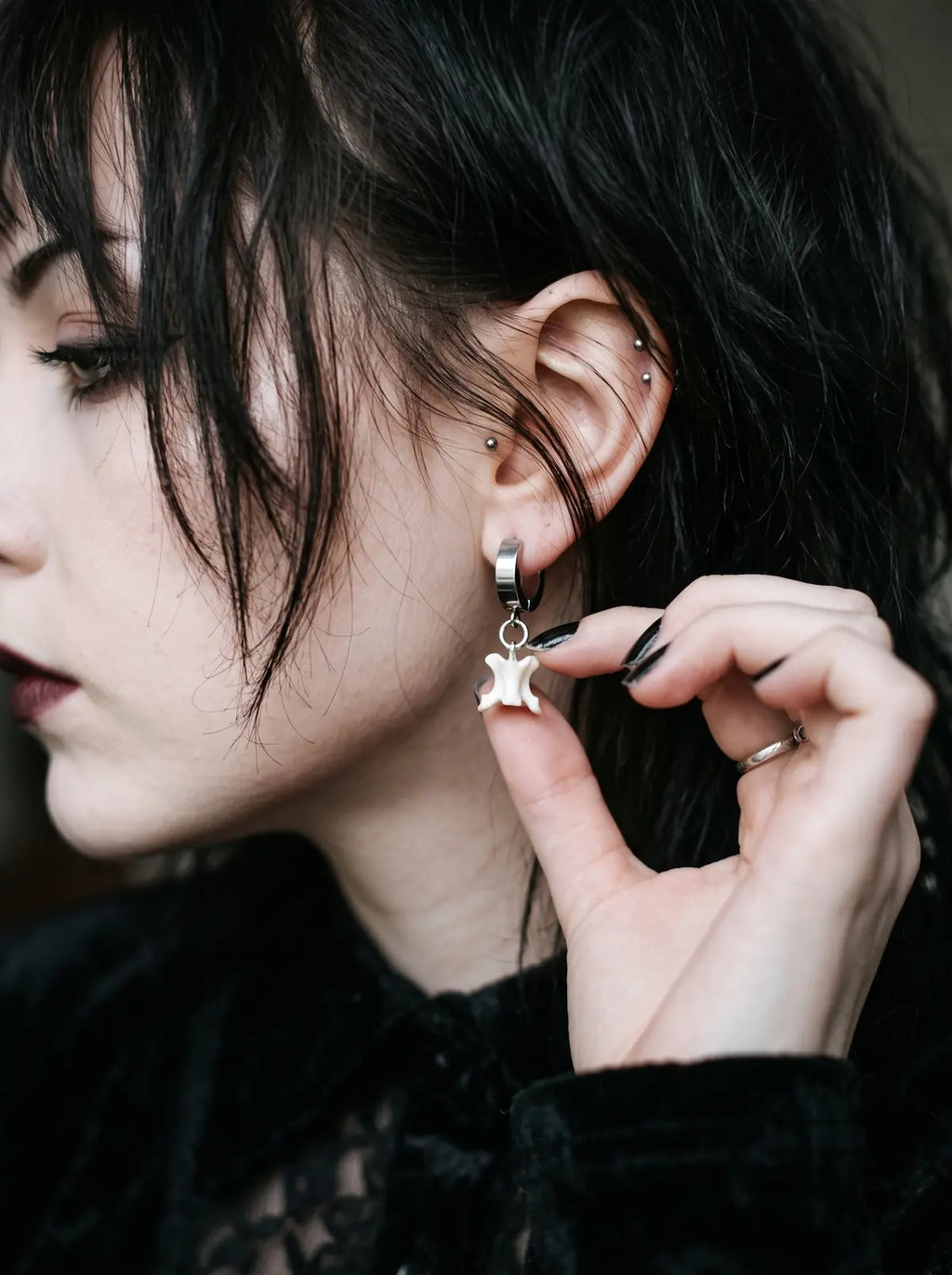 Ivory Vertebra Drop snake bone clip-on earring worn with a finger touching the dangling vertebra
