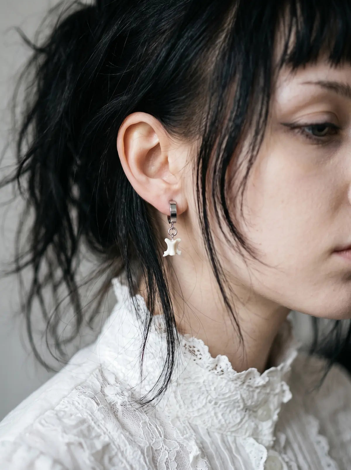 Ivory Vertebra Drop snake bone clip-on earring shown in profile above a white lace collar