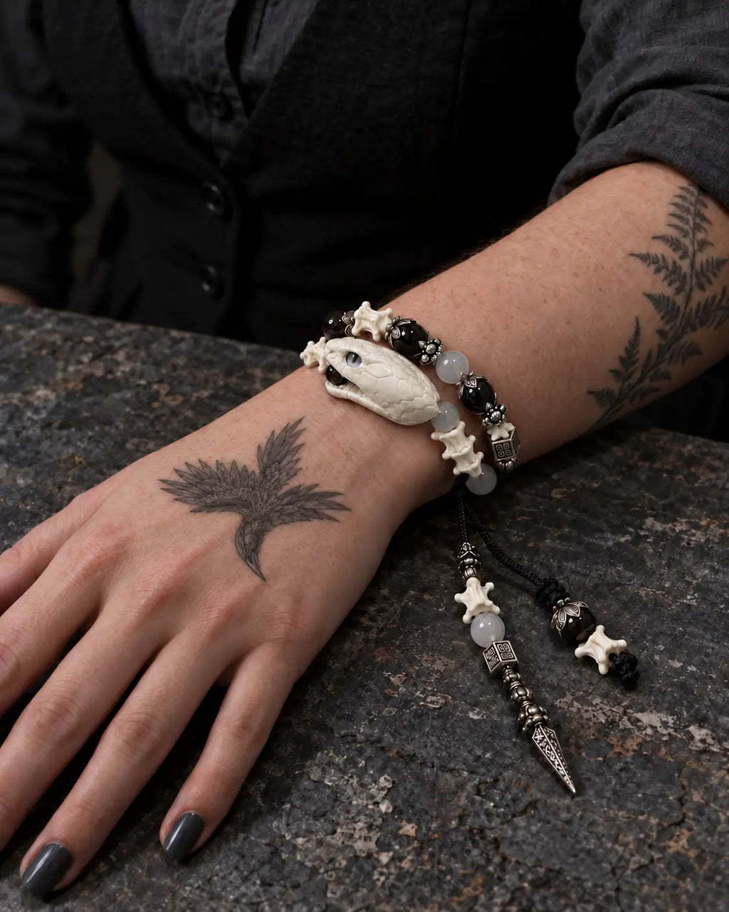 Ivory Serpent Head snake bone bracelet on a wrist resting on a dark tabletop, with its pointed pendant beside the hand