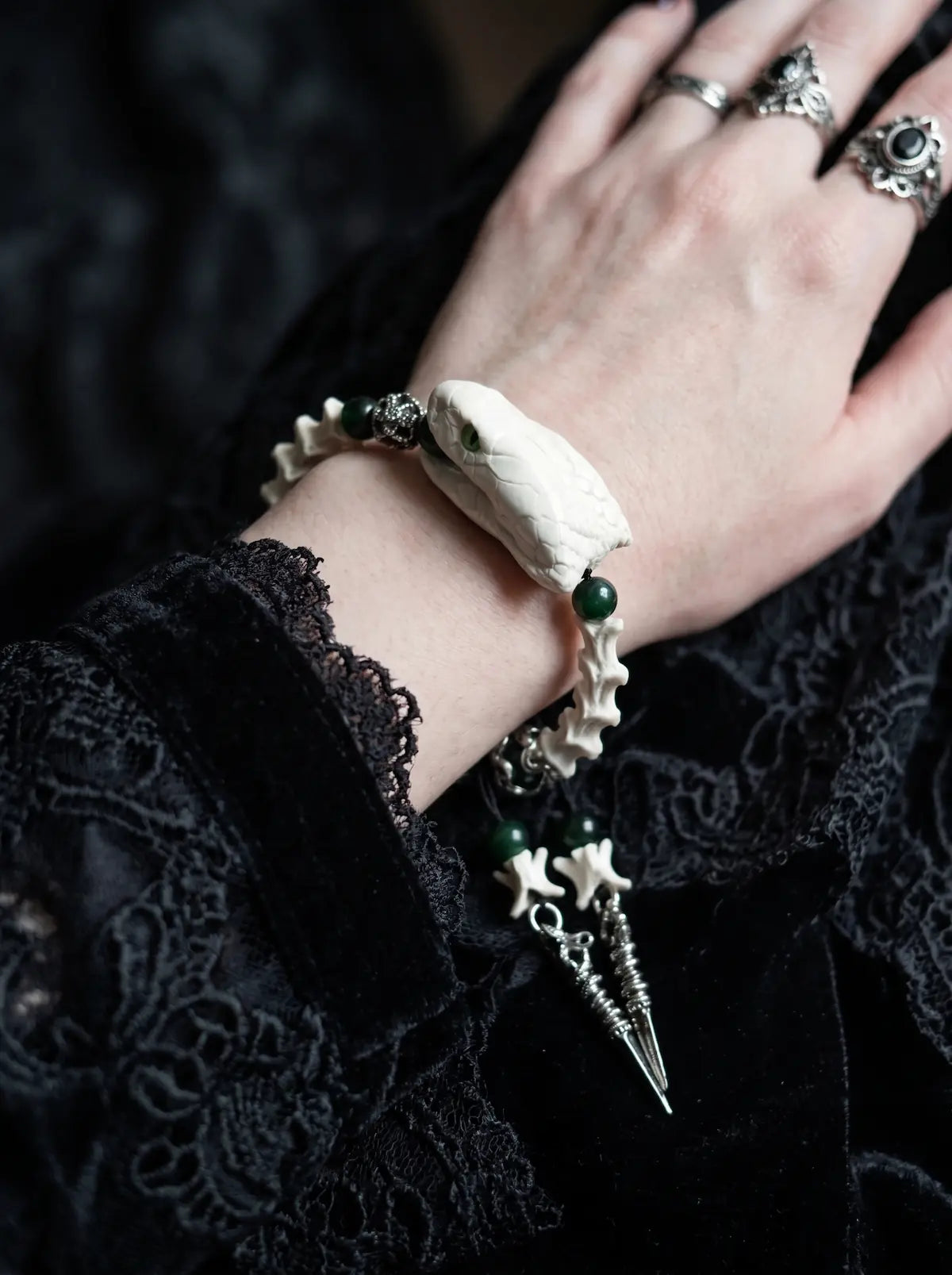 Jadefang Snake Bone Bracelet, snake head and green bead bracelet worn on the back of a hand with rings