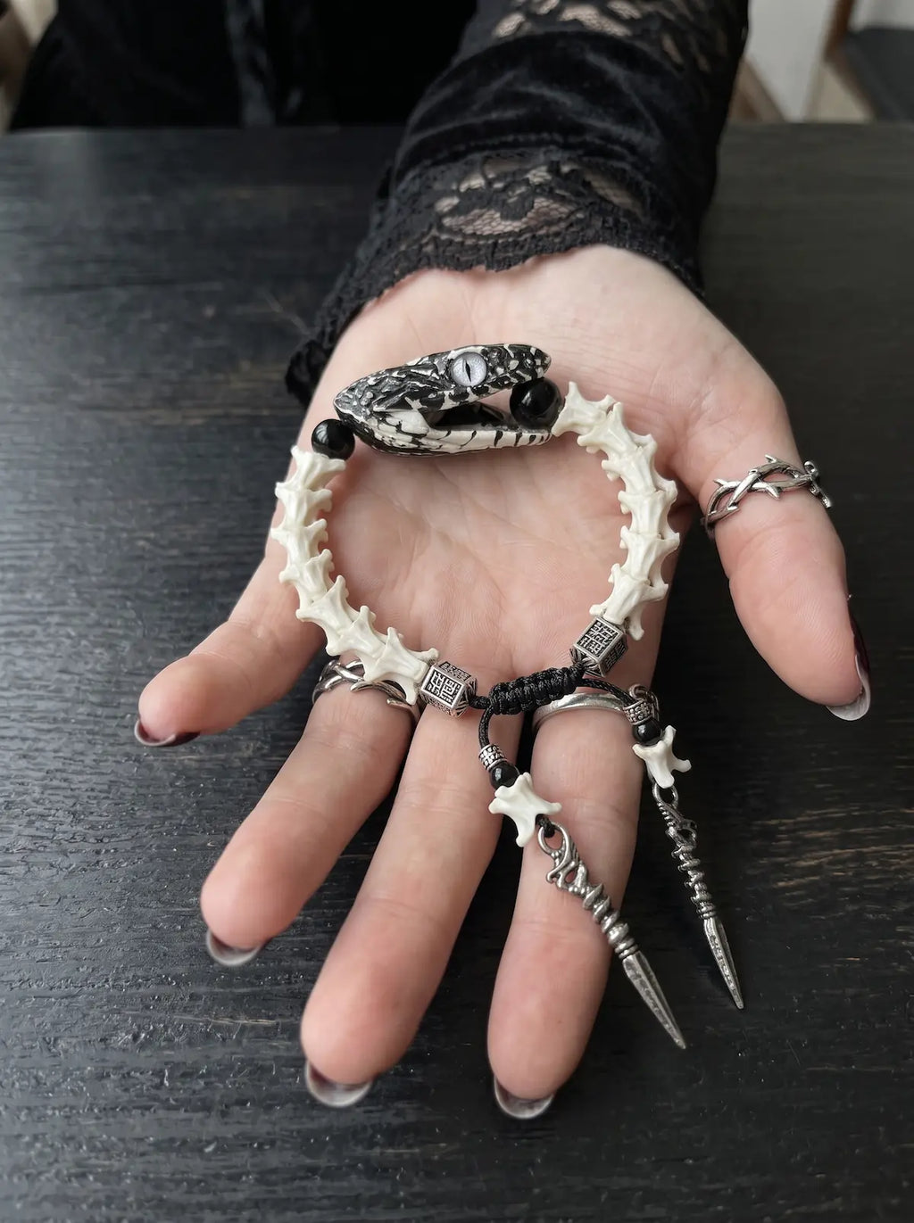 Kingshade Snake Bone Bracelet, pale snake bone bracelet resting in an open palm with two dangling metal drops