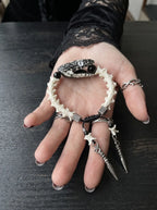 Kingshade Snake Bone Bracelet, pale snake bone bracelet resting in an open palm with two dangling metal drops