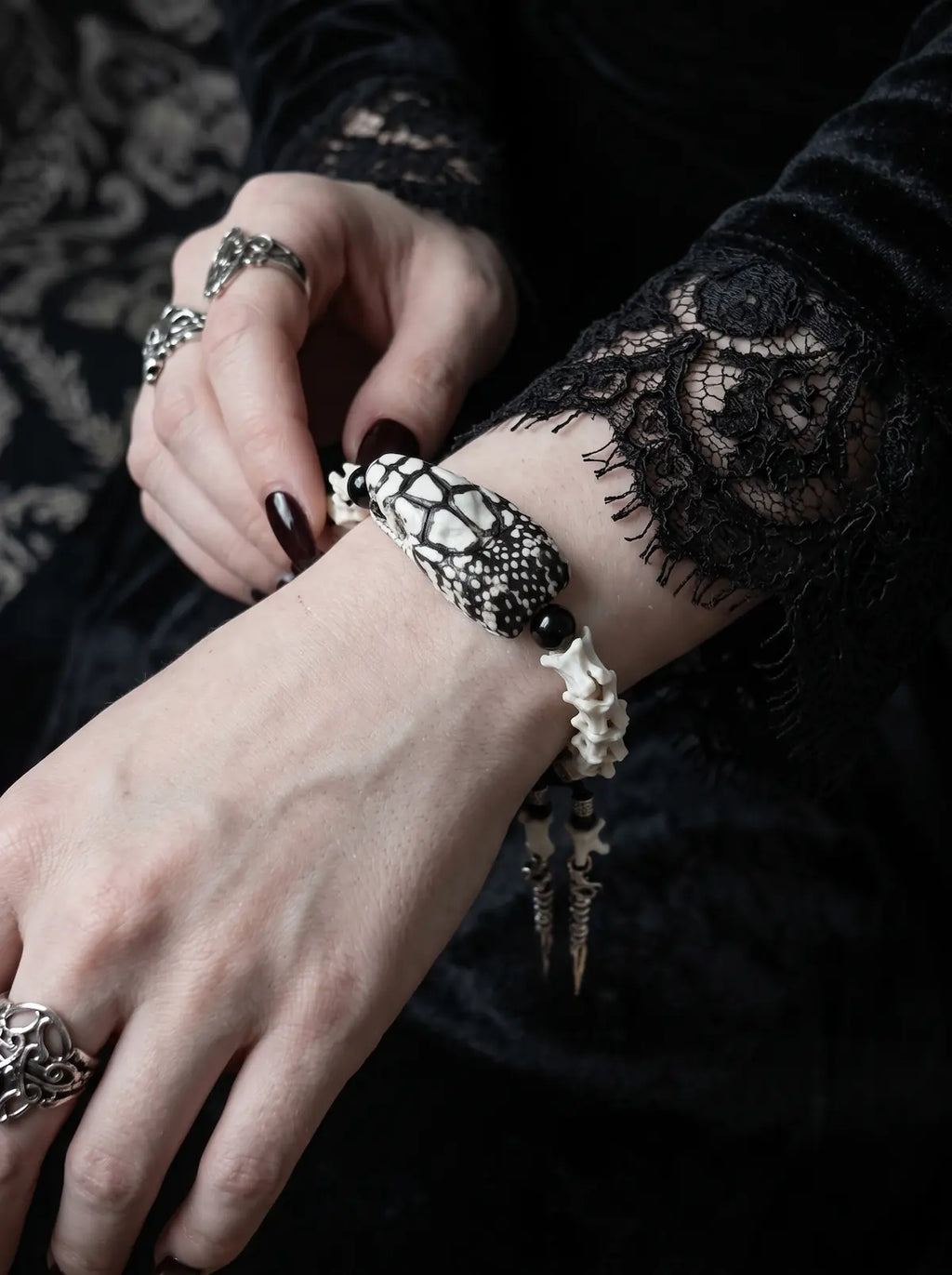 Kingshade Snake Bone Bracelet, snake head and vertebrae bracelet in close view beside black lace and silver rings