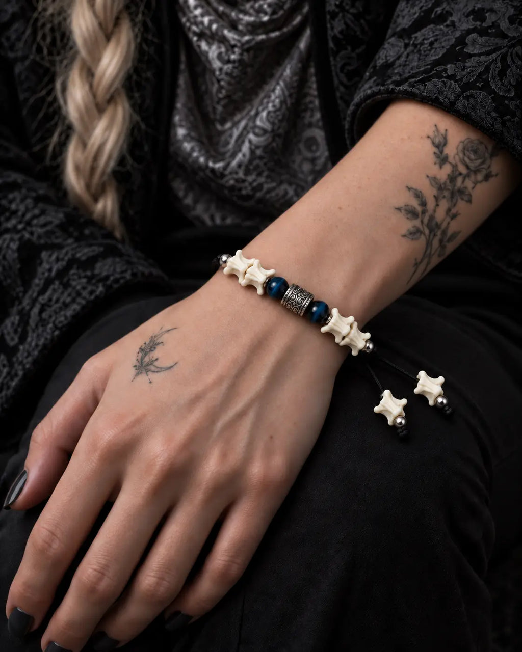 Midnight Blue snake bone bracelet worn on a hand resting on the thigh, with white bone-tipped cords beside the wrist