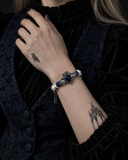Midnight Guardian snake bone bracelet worn with the hand at a black ruffled collar beside a blue brocade vest