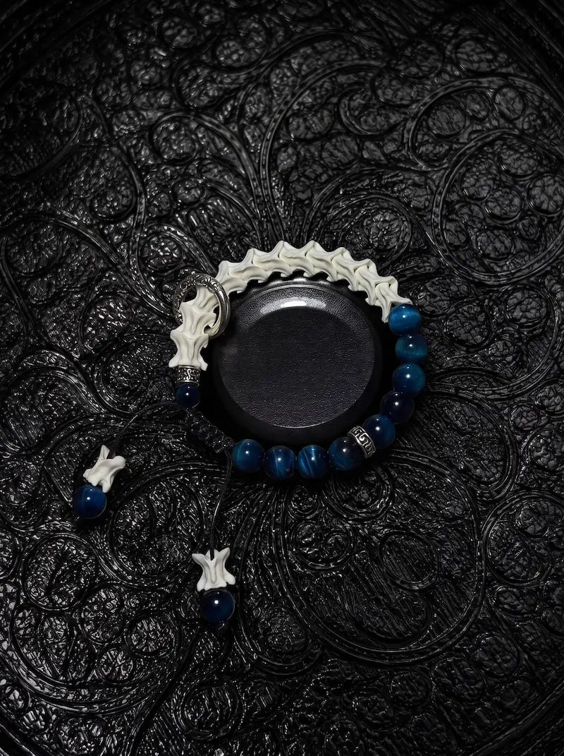 Midnight Halo snake bone bracelet with blue beads, an engraved silver-tone ring and bone-tipped cords on a black stand