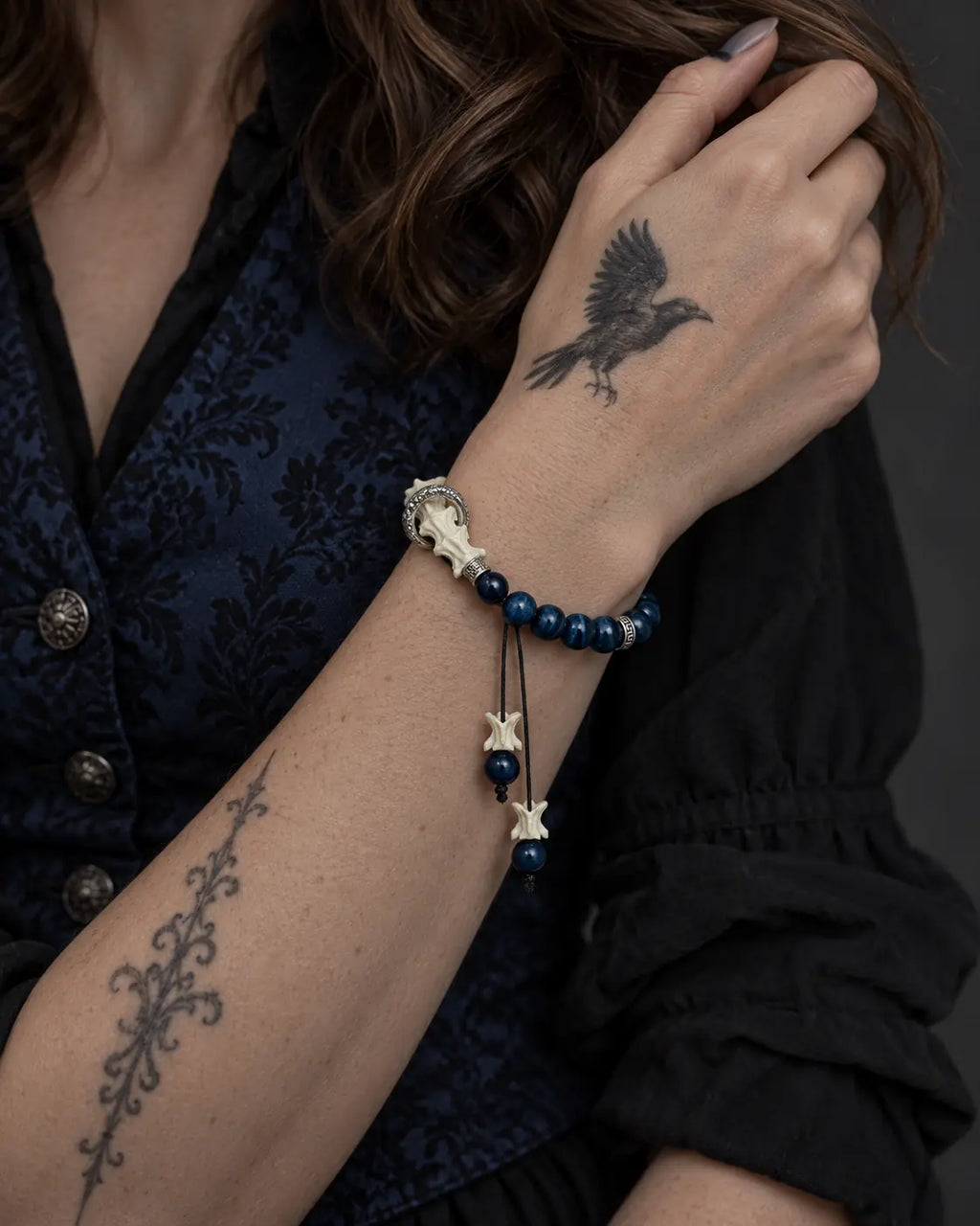 Midnight Halo snake bone bracelet worn with the hand at the opposite shoulder above a blue brocade vest