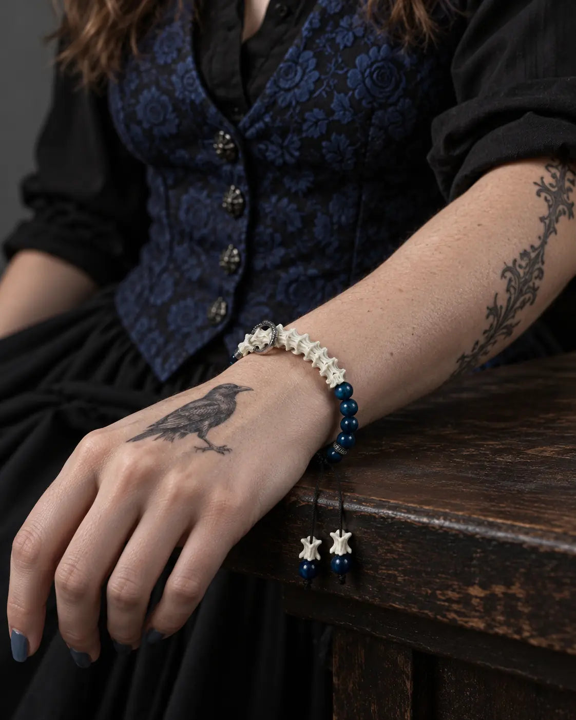 Midnight Halo snake bone bracelet on a wrist resting on a wooden table, with its two bone- and bead-tipped cords hanging down
