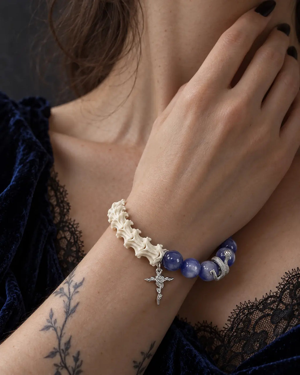 Midnight Serpent Cross snake bone bracelet worn with the hand near the neck above a black lace neckline