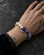 Midnight Serpent Cross snake bone bracelet on a wrist resting on a dark stone surface beside a blue velvet sleeve