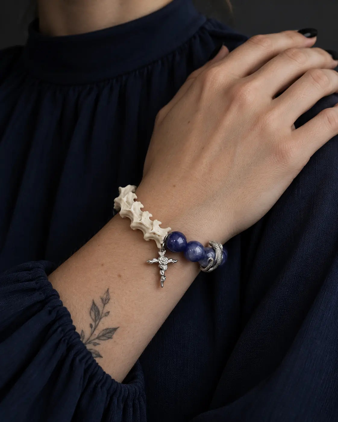 Midnight Serpent Cross snake bone bracelet worn with the hand resting on the opposite shoulder over a navy blouse