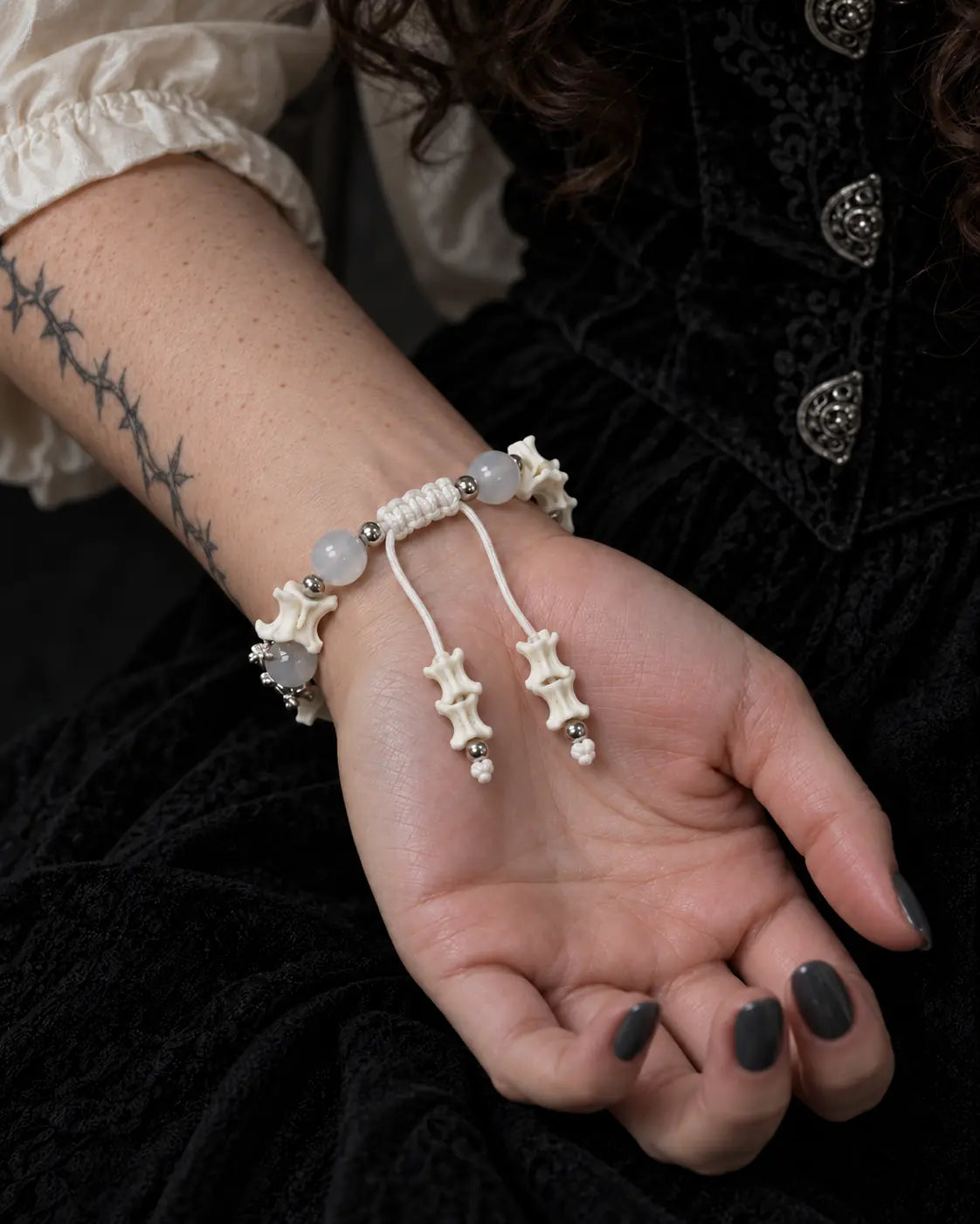 Palm-up view of the Moon Serpent snake bone bracelet showing its white sliding knot and two vertebra-tipped cord ends