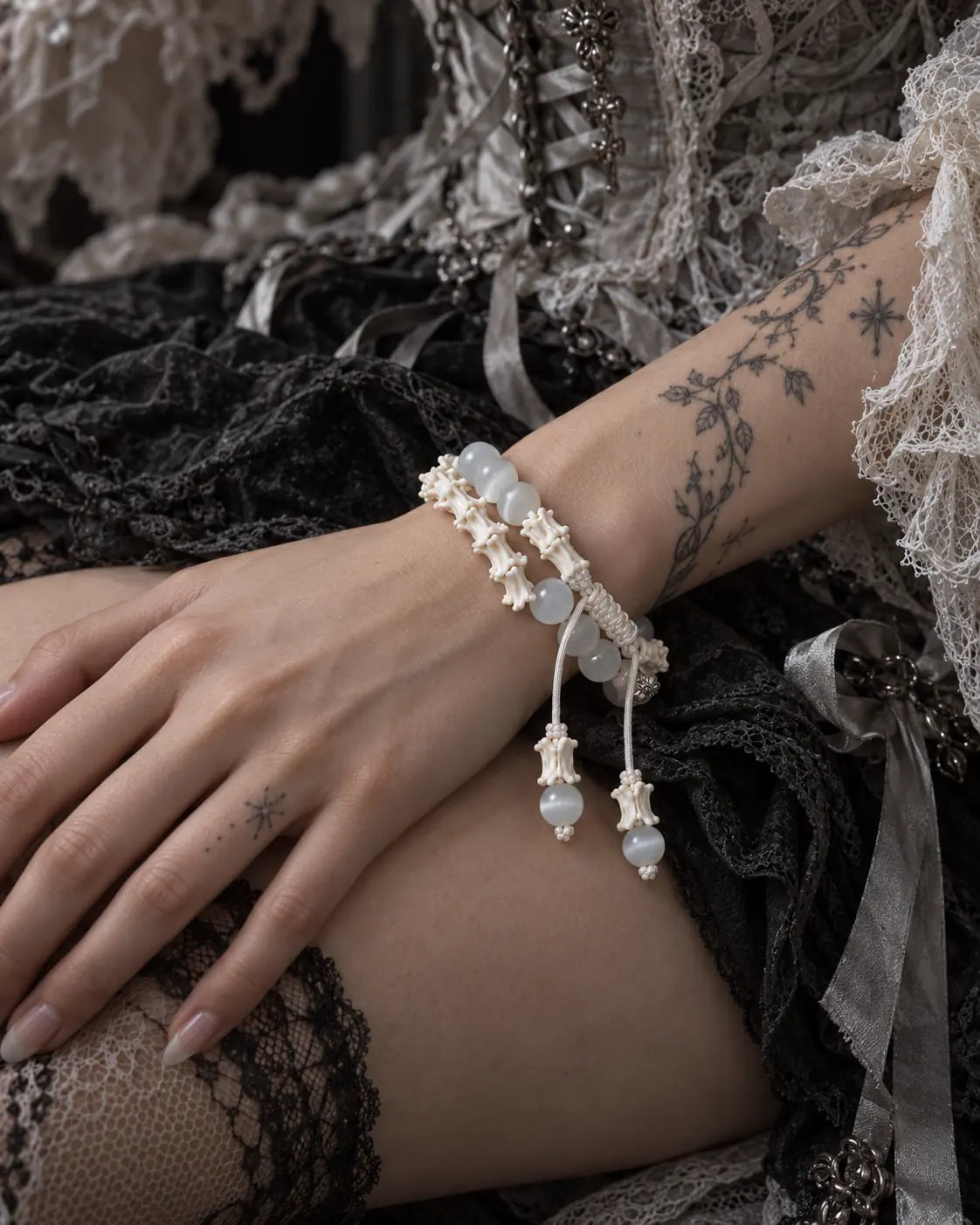 Moonveil snake bone bracelet shown across a wrist above black fabric, with two beaded cord ends hanging down