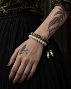 Mosswood snake bone bracelet on a hand resting against a black skirt beneath an olive velvet sleeve