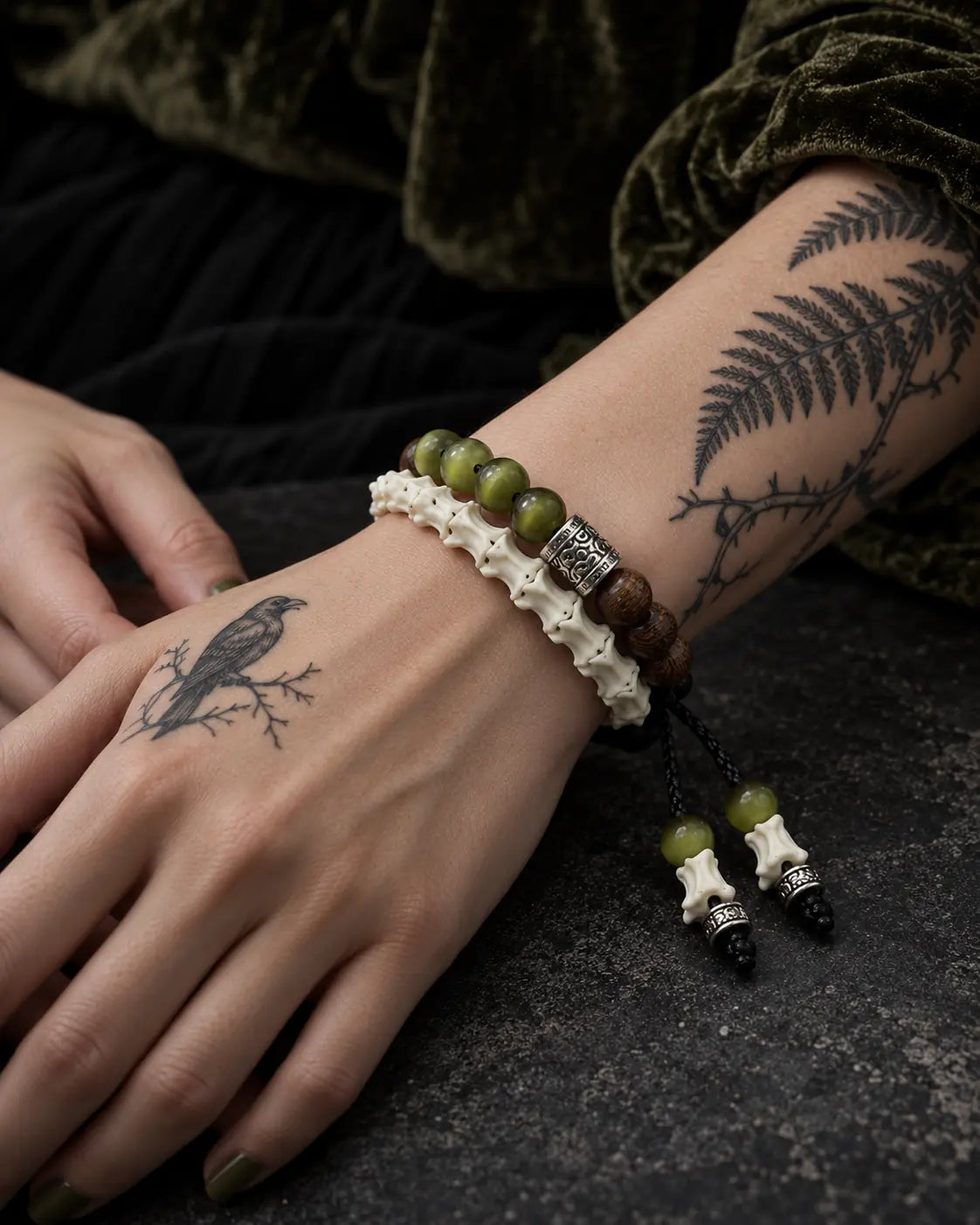 Close-up of the Mosswood snake bone bracelet showing green and brown beads, engraved spacers and dangling bone tips