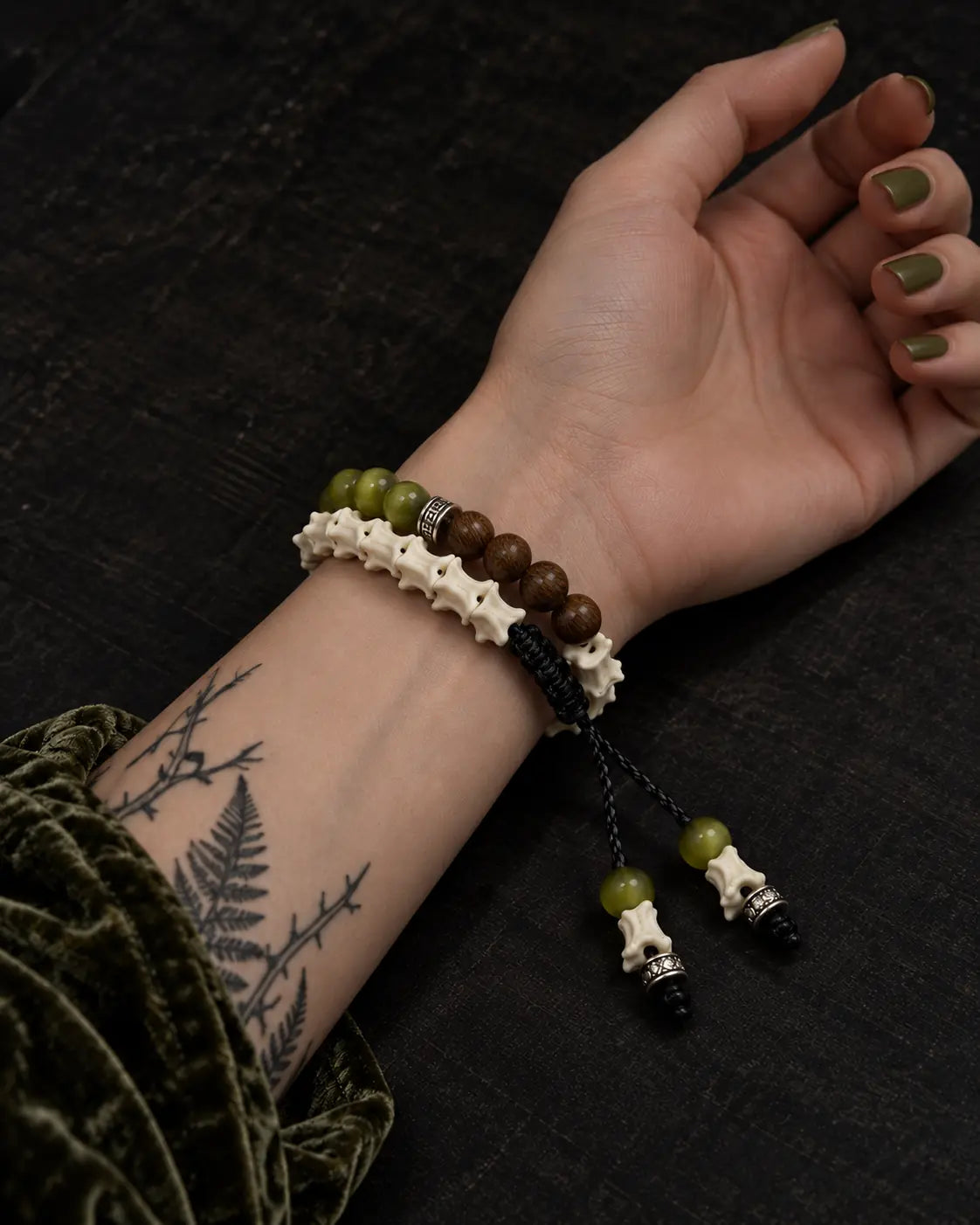 Palm-up view of the Mosswood snake bone bracelet showing layered rows, a black knot and two beaded cord ends
