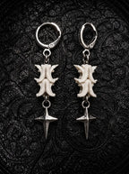 Nightstar snake bone earrings with white vertebrae and silver-tone four-point star drops on black patterned fabric