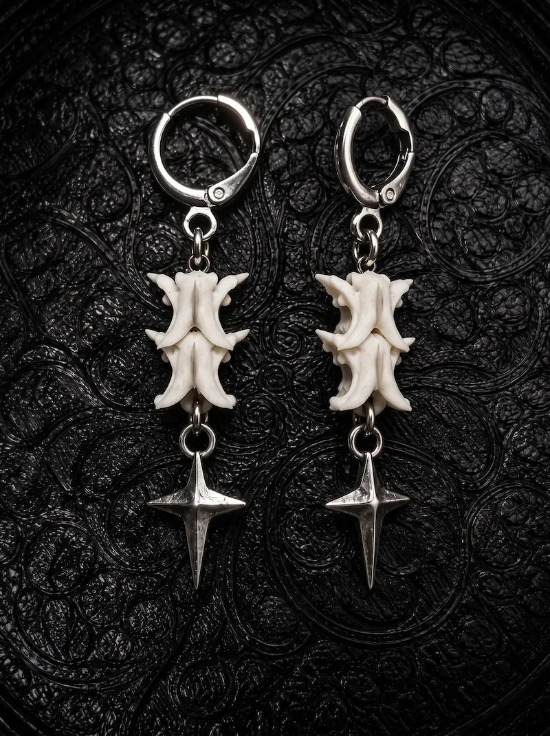 Nightstar snake bone earrings with white vertebrae and silver-tone four-point star drops on black patterned fabric