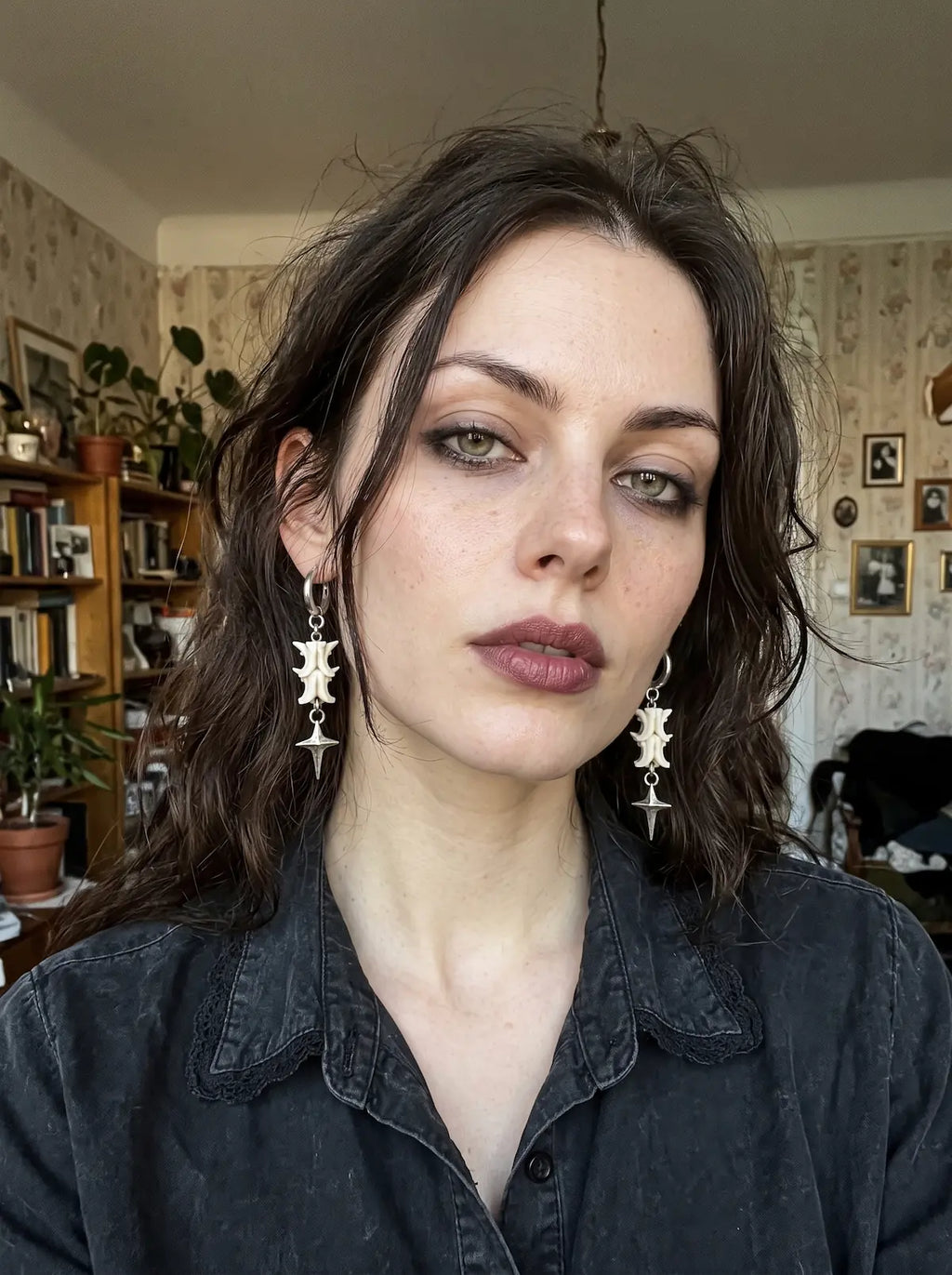 Nightstar snake bone drop earrings worn as a pair with a dark button-front shirt