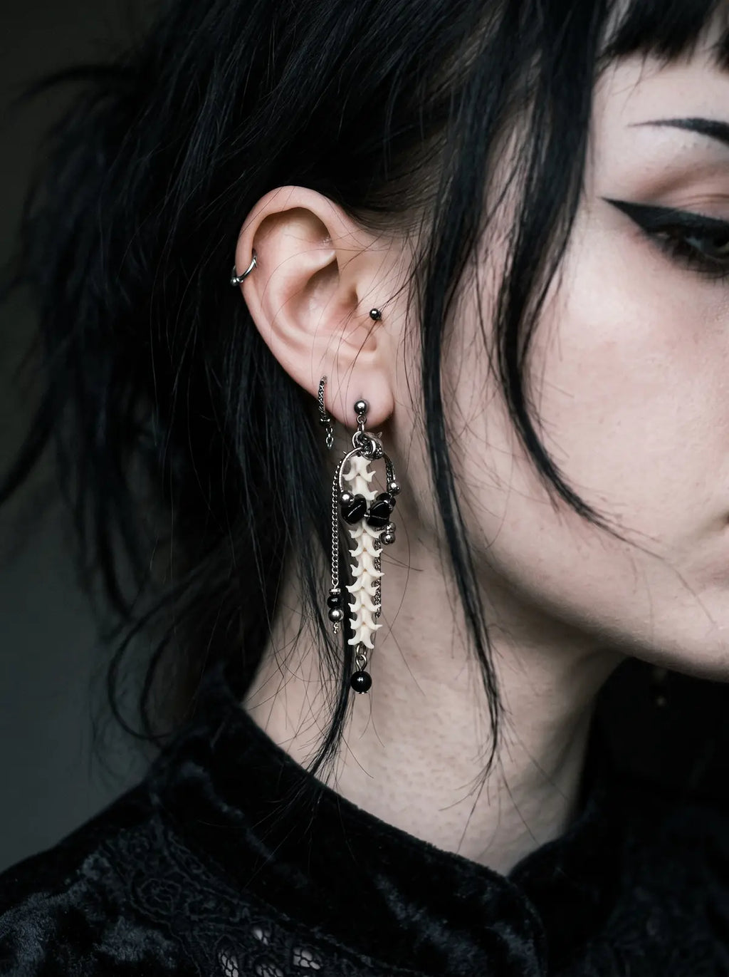 Nocturne Arc Snake Bone Earrings, long vertebrae earring worn against short black hair in a close side portrait