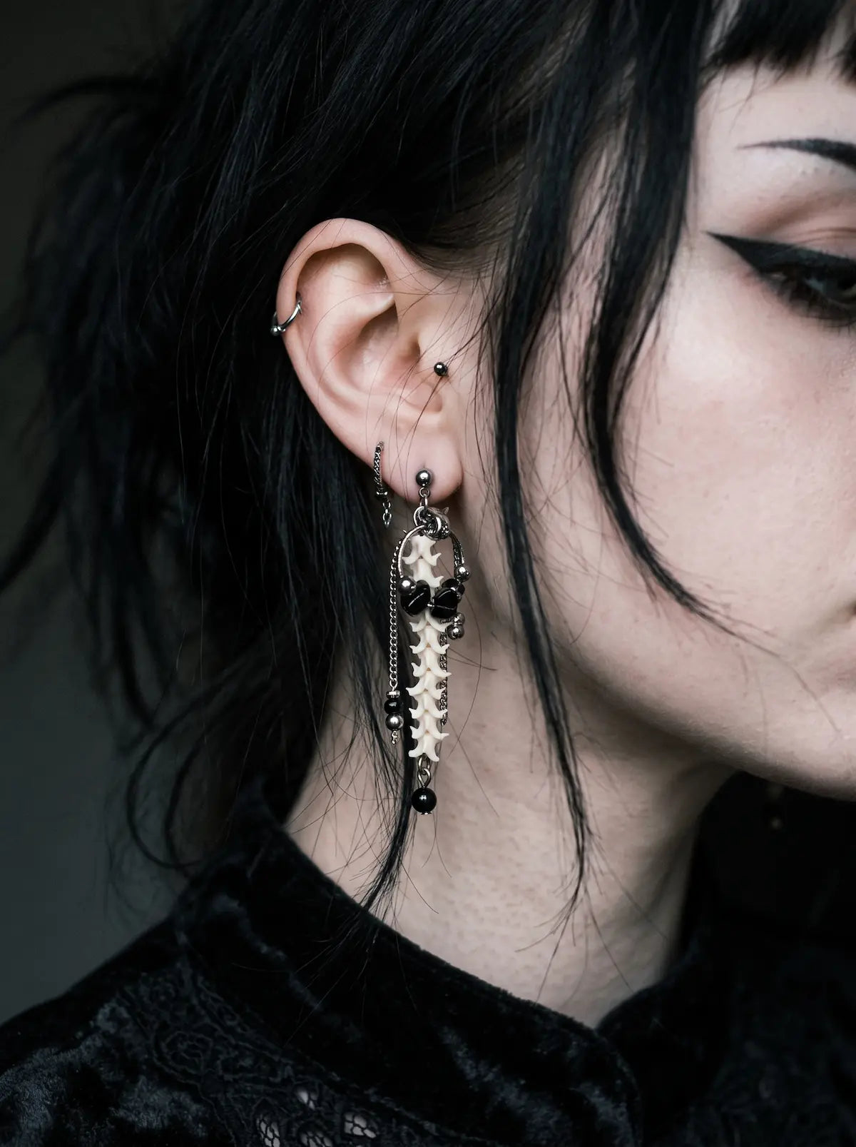 Nocturne Arc Snake Bone Earrings, long vertebrae earring worn against short black hair in a close side portrait
