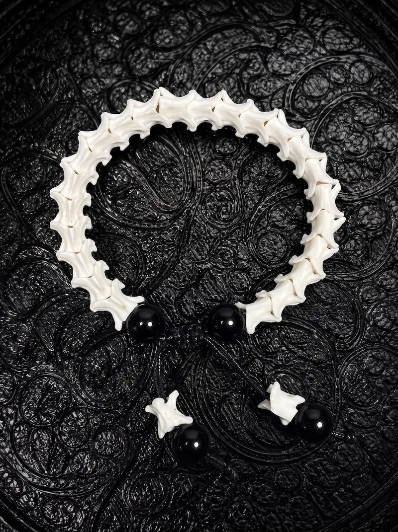 Noir Spine snake bone bracelet with glossy black beads, a black sliding knot and bone-tipped cords on patterned fabric