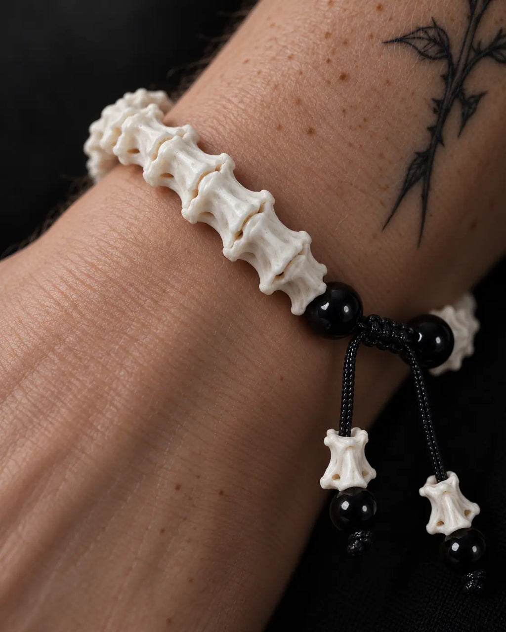 Macro view of the Noir Spine snake bone bracelet showing the vertebrae, glossy black beads and braided cord closure