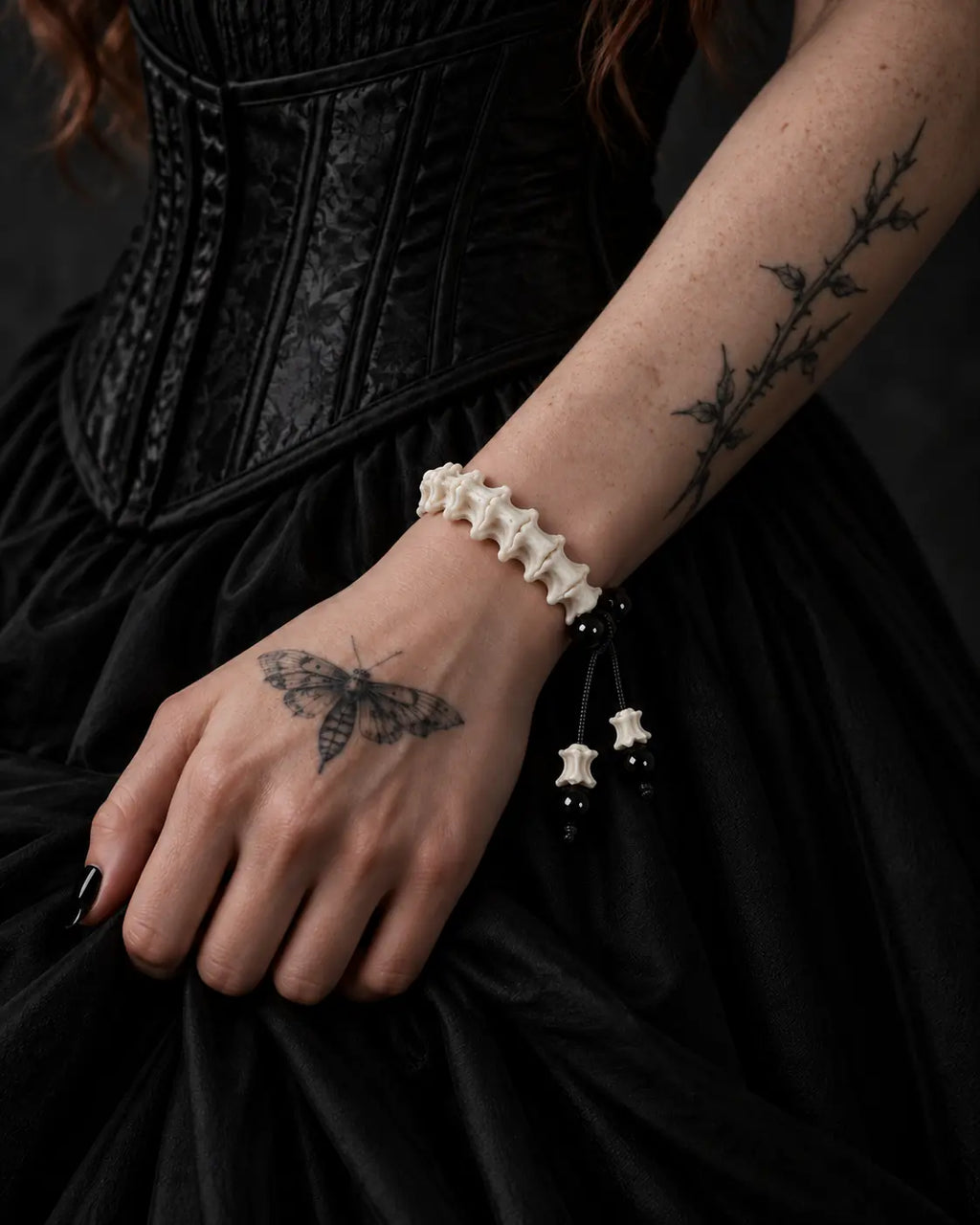 Noir Spine snake bone bracelet on a wrist resting against a black skirt below a corset