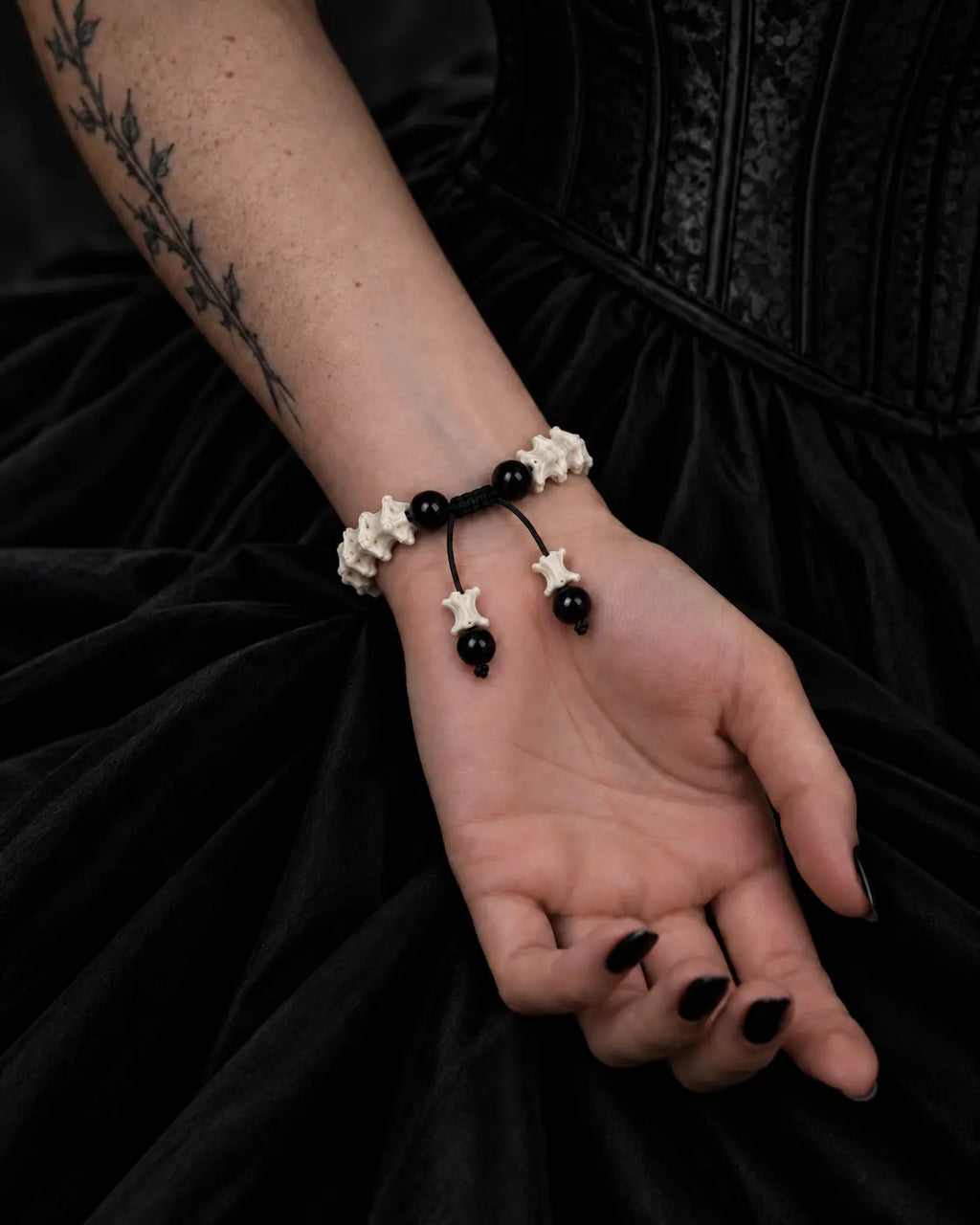 Palm-up view of the Noir Spine snake bone bracelet showing black beads, a sliding knot and two bone-tipped cords