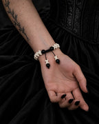 Palm-up view of the Noir Spine snake bone bracelet showing black beads, a sliding knot and two bone-tipped cords