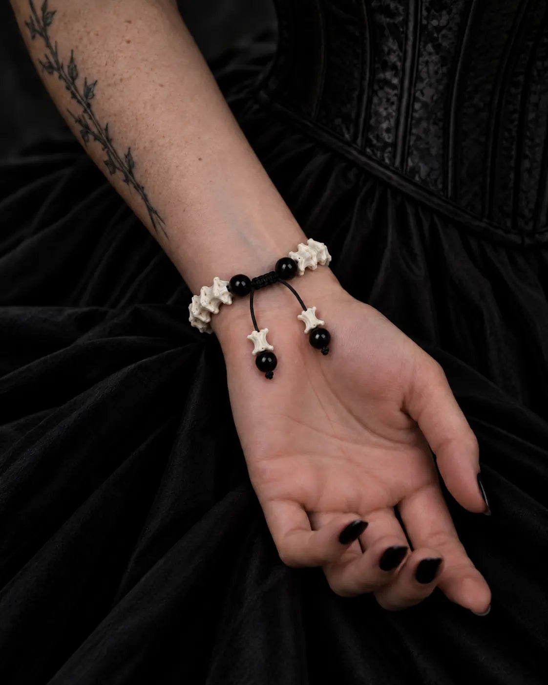Palm-up view of the Noir Spine snake bone bracelet showing black beads, a sliding knot and two bone-tipped cords
