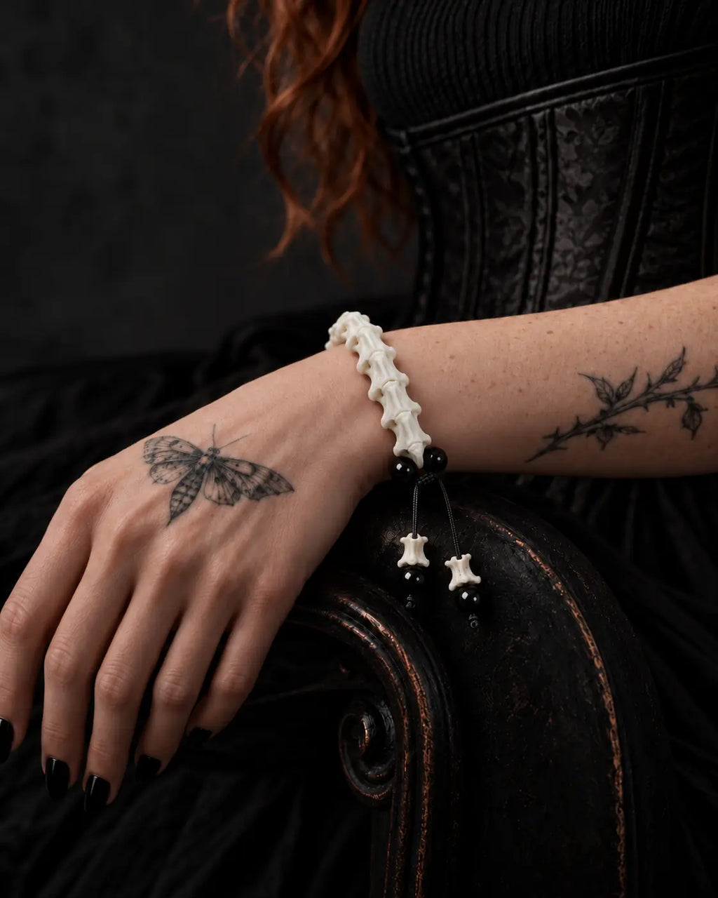 Noir Spine snake bone bracelet on a hand resting over the carved wooden arm of a dark chair