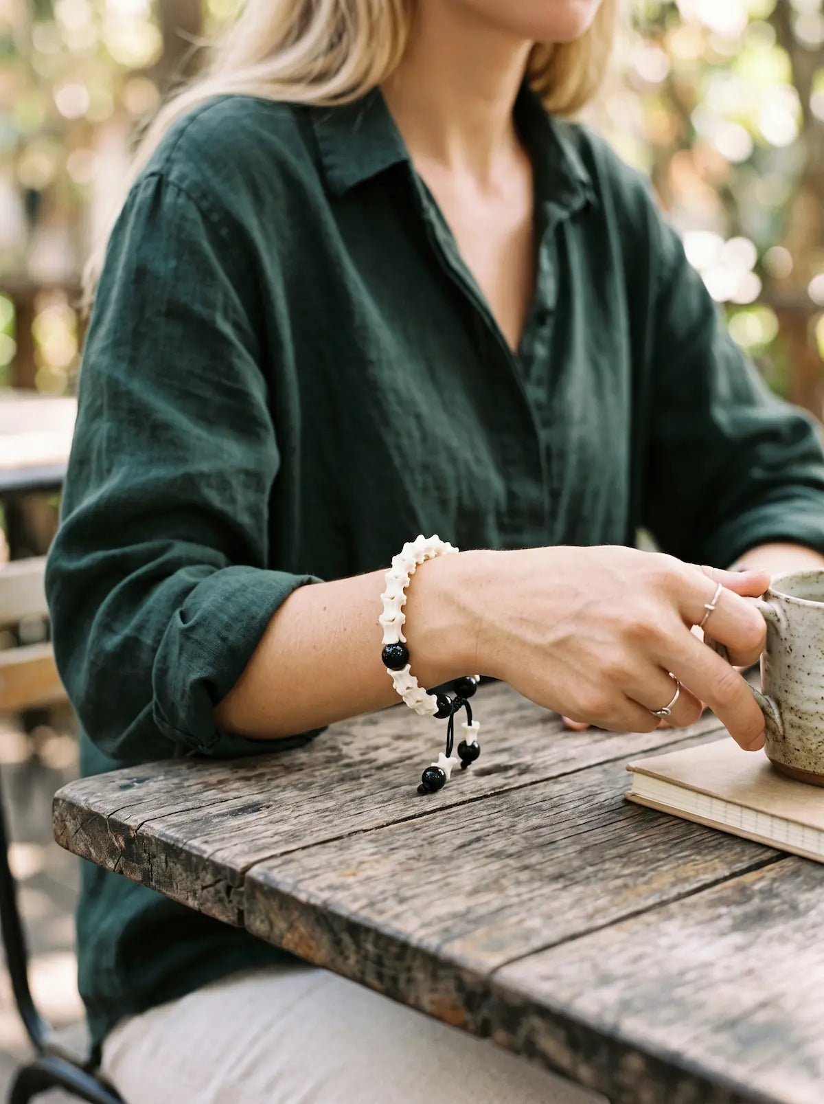 Noir Spine snake bone bracelet worn while holding a cup at an outdoor wooden table